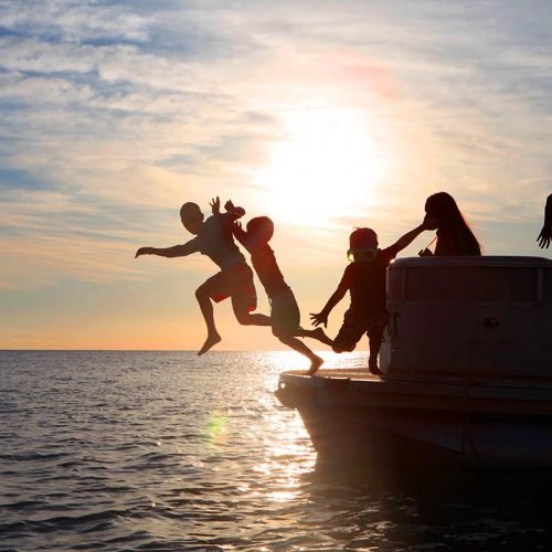 Kids jumping off a boat at sunset